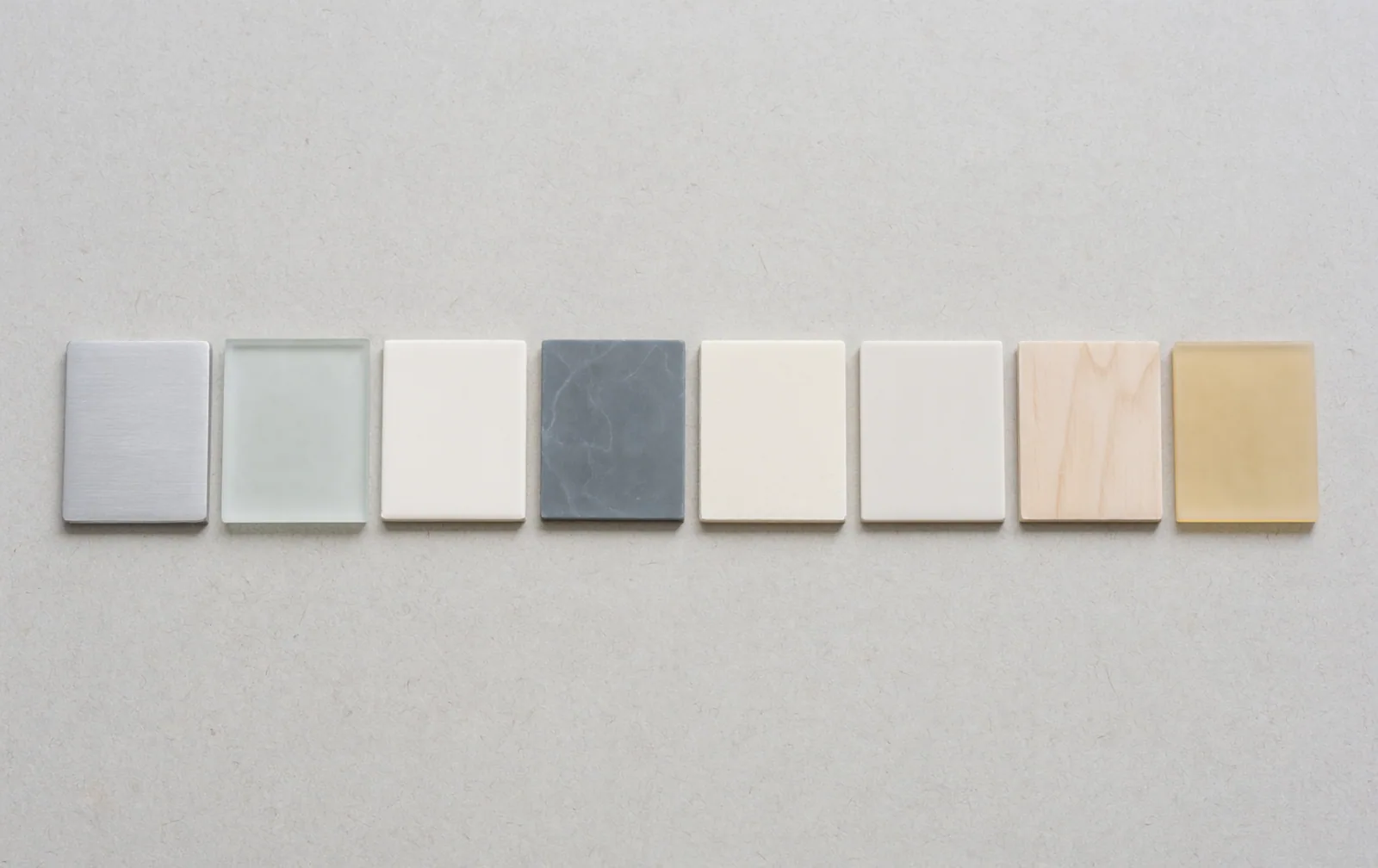 Eight small flat tiles of different pale materials laid out in an evenly spaced row.