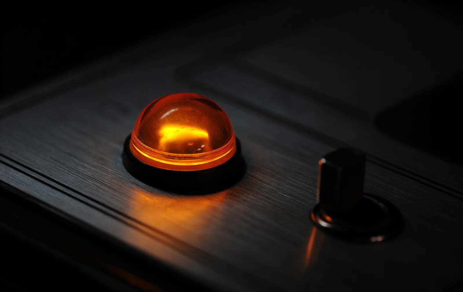 A single amber indicator lamp lit on a dark instrument panel in an otherwise black room.
