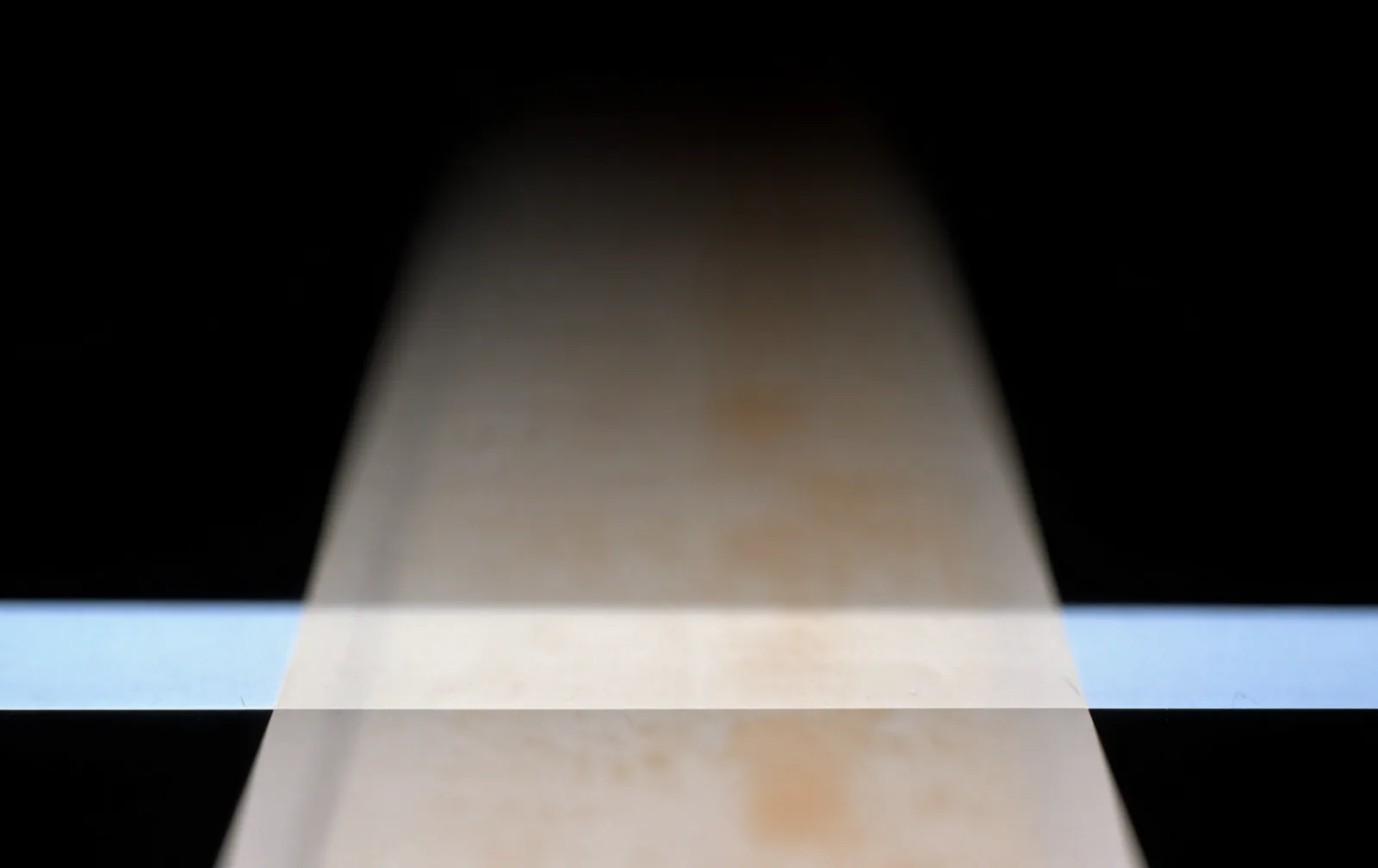 A pale strip receding into blackness, stained and out of focus, crossed by one narrow band of cold light.