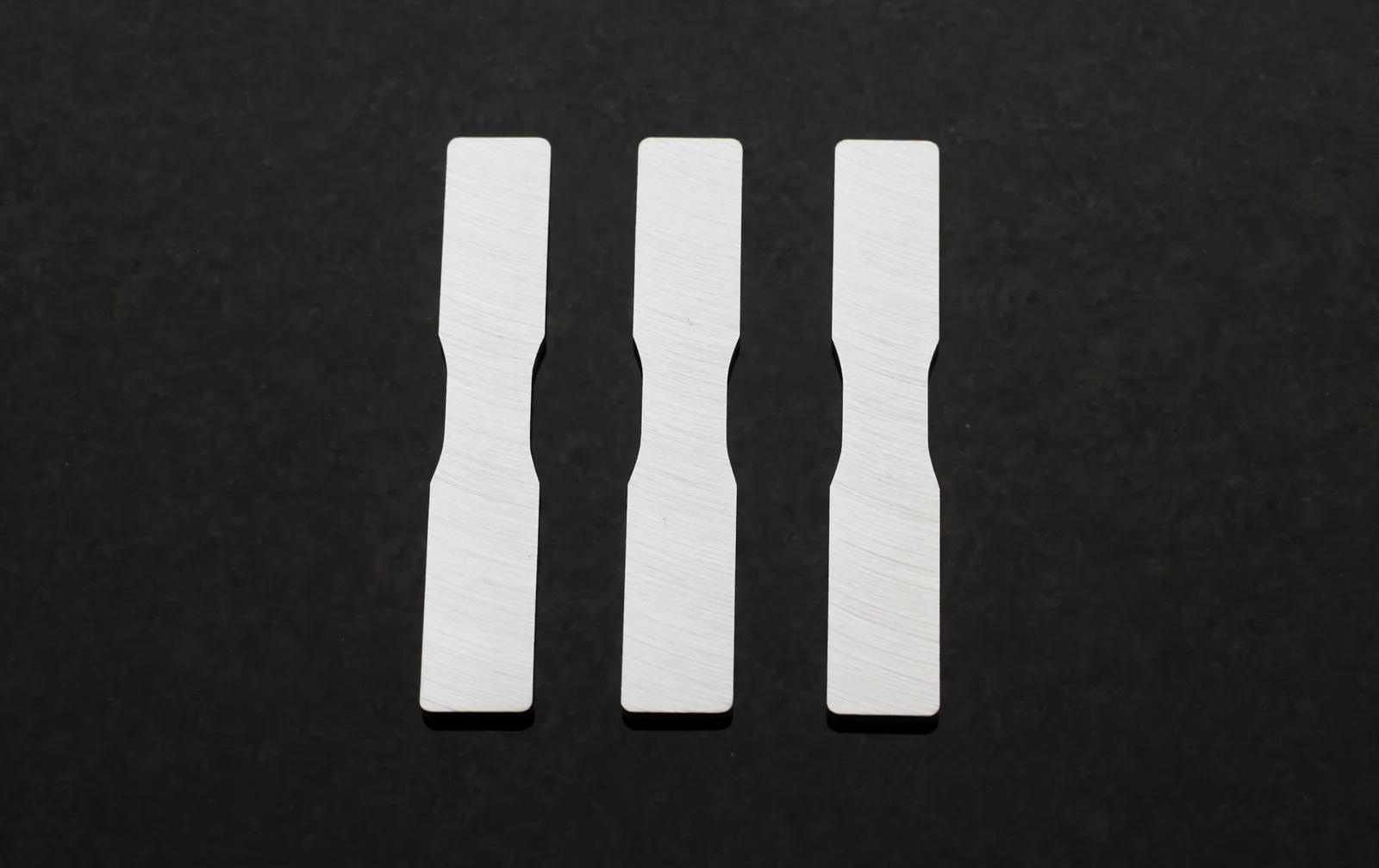Three identical machined metal test coupons laid out in a row on black granite.
